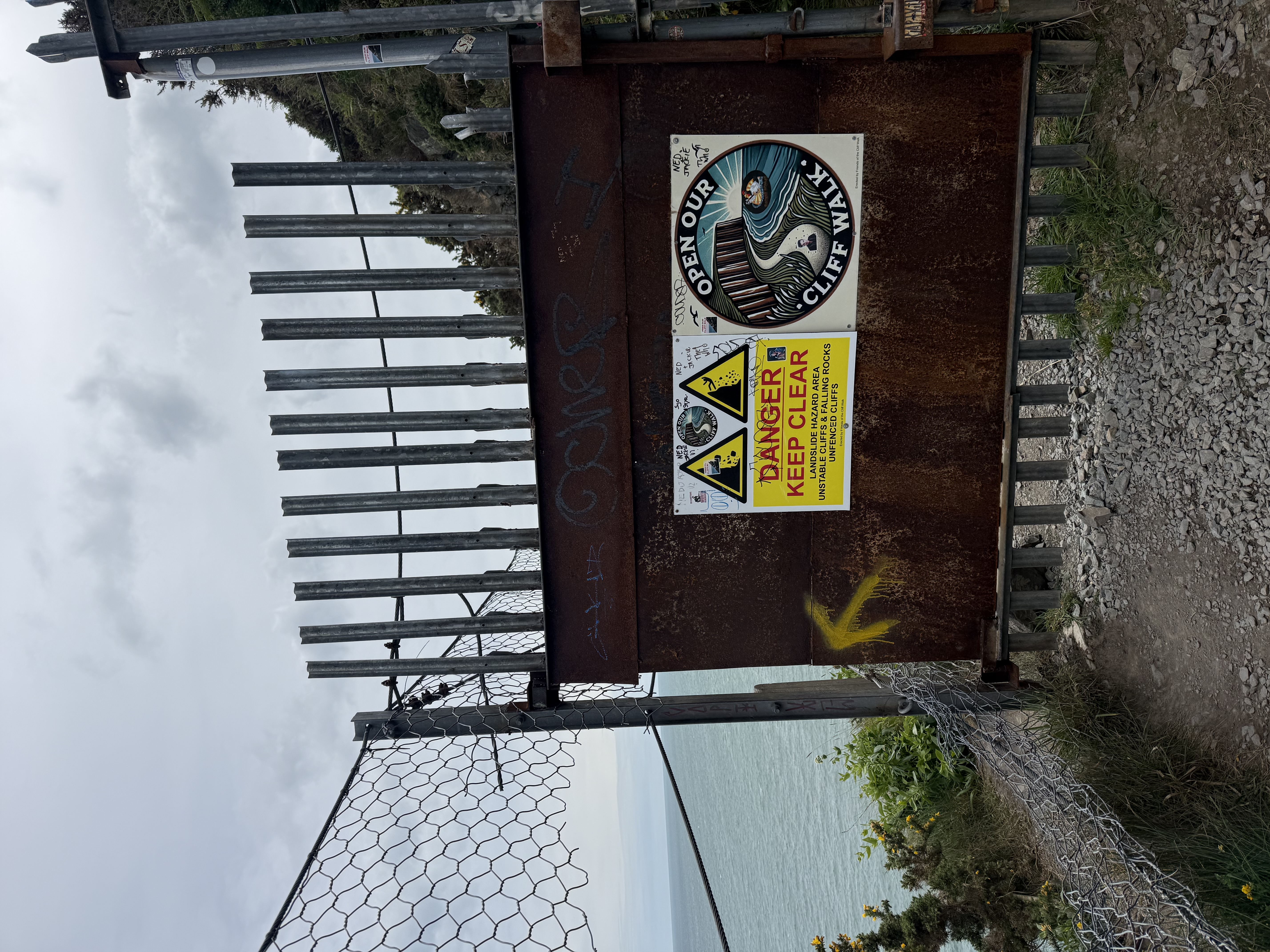 a fence saying closed with a yellow arrow pointing to a hole in the fence