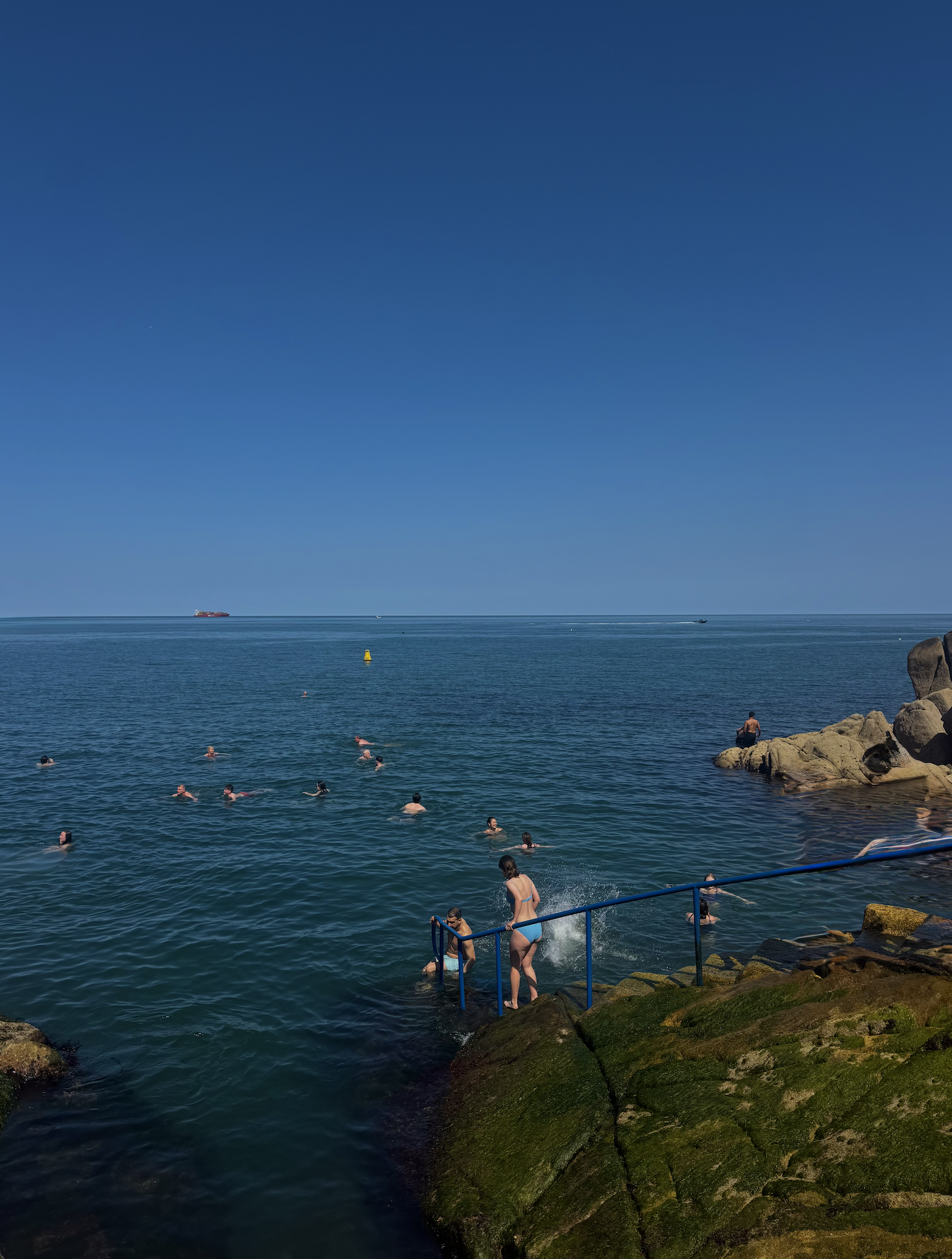 a bunch of people swimming in the water next to a rocky shoreline